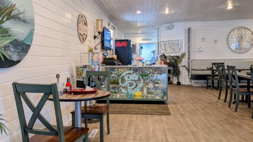 Cozy restaurant interior with a colorful counter, tables, and decor featuring plants and artwork on white walls.