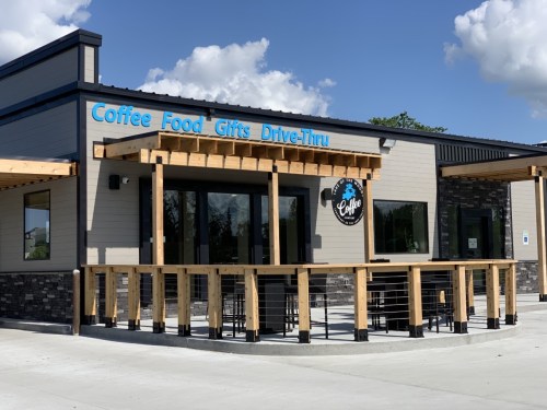Exterior of a modern coffee shop with a drive-thru, featuring a wooden deck and blue signage.