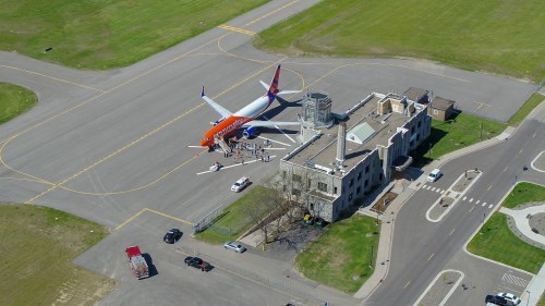 Aerial view of an orange and white airplane parked at an airport near a historic building and green grass.