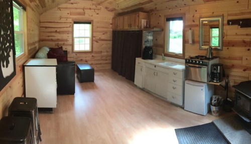 Cozy wooden cabin interior featuring a kitchen, seating area, and large windows for natural light.