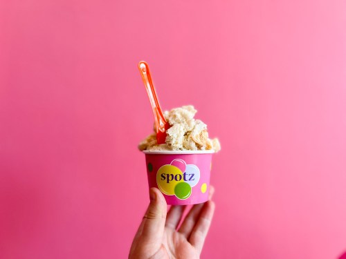 A hand holding a colorful cup of ice cream with a bright pink background.