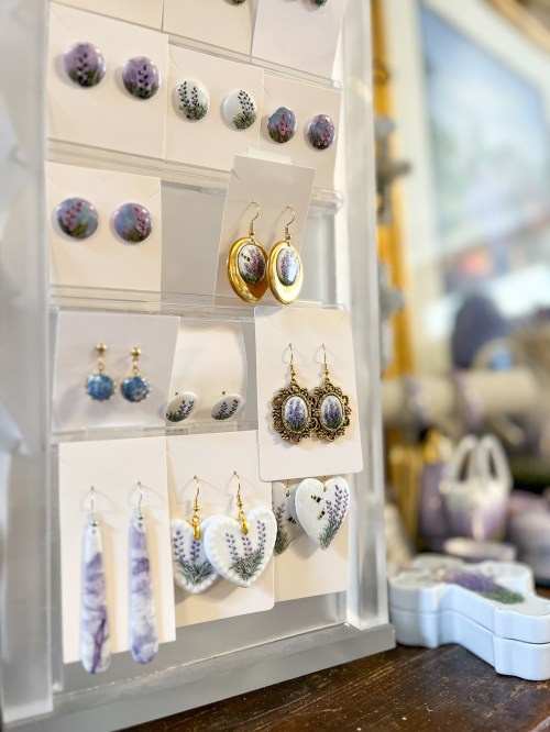 A display of various earrings and studs, featuring floral designs and different shapes, on a white stand.