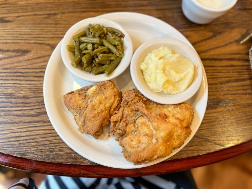 A plate with two pieces of fried chicken, mashed potatoes, and green beans on a wooden table.