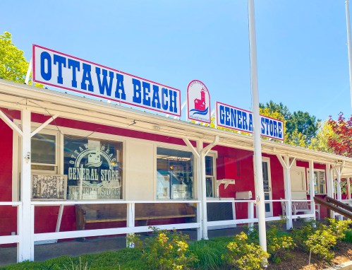 Exterior of Ottawa Beach General Store, featuring a bright red facade and a blue sign with white lettering.