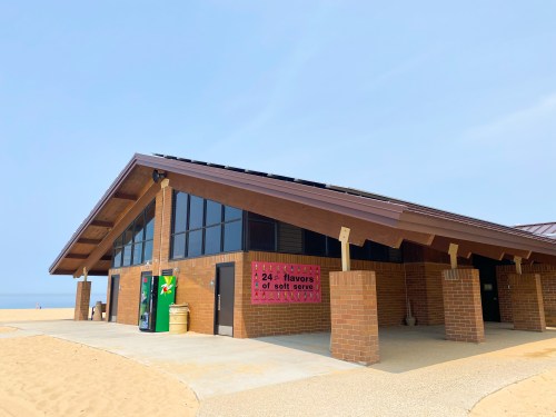 A beachside building with large windows, featuring a sign for "24 flavors of soft serve" and vending machines outside.