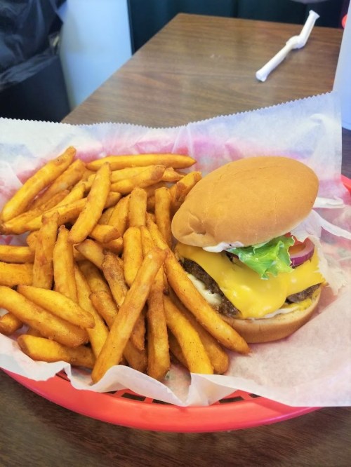 A cheeseburger with lettuce, tomato, and pickles served with a side of golden French fries on a red tray.
