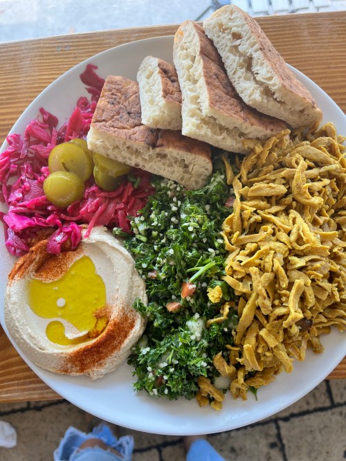 A plate of Middle Eastern food featuring hummus, tabbouleh, pickled vegetables, olives, and pita bread.