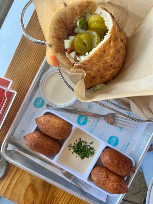 A pita filled with pickles and vegetables, served with four fried balls and a dipping sauce on a tray.