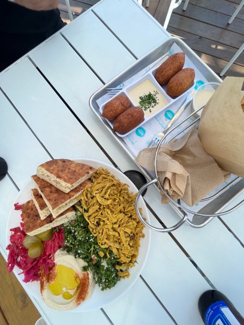 A plate of food featuring flatbread, shredded chicken, salad, pickles, and a side of fried snacks on a table.