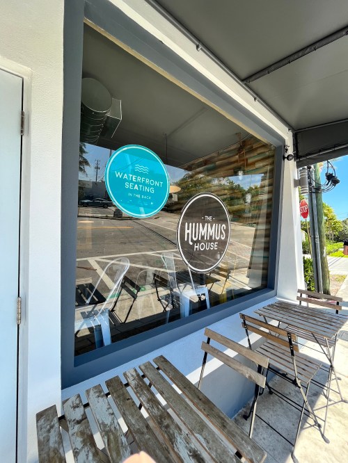 A restaurant window displaying signs for "Waterfront Seating" and "The Hummus House," with outdoor seating visible.