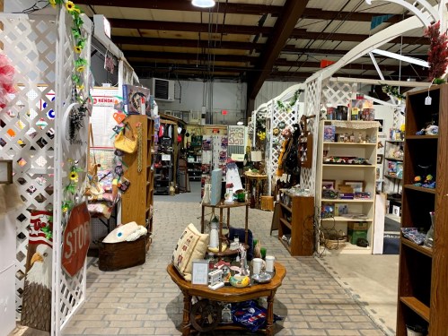 A spacious indoor market with wooden displays, decorative items, and various goods for sale along a brick pathway.