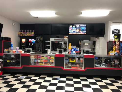 A concession stand with a black and red design, featuring snacks, drinks, and a menu display. Black and white checkered floor.