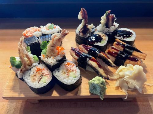 A wooden platter featuring various sushi rolls, including eel, tempura, and garnishes of wasabi and pickled ginger.