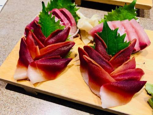 A beautifully arranged platter of sushi featuring rose-shaped slices of fish and garnished with green leaves.
