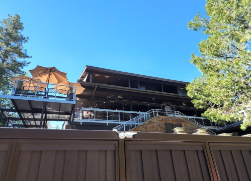 A modern building with a balcony and patio, surrounded by trees under a clear blue sky.