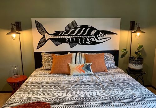 A cozy bedroom featuring a bed with patterned bedding, a large fish mural above, and stylish wall sconces.