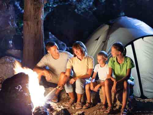 A family sits around a campfire at night, enjoying each other's company near a tent.