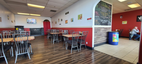 A spacious restaurant interior with red walls, wooden floors, tables, and chairs, featuring a chalkboard menu and TV.