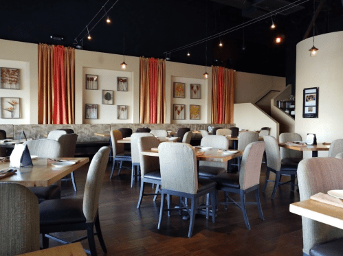A modern restaurant interior with wooden tables, upholstered chairs, and framed artwork on the walls.