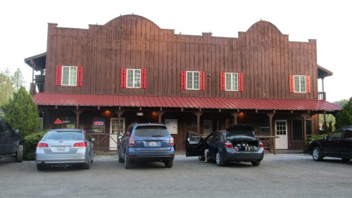 A rustic wooden building with red shutters and a metal roof, featuring parked cars in front.