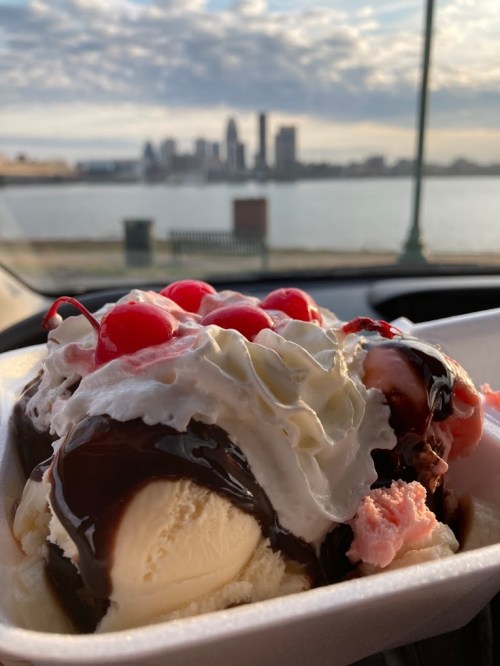 A close-up of a sundae topped with cherries and whipped cream, with a city skyline and water in the background.