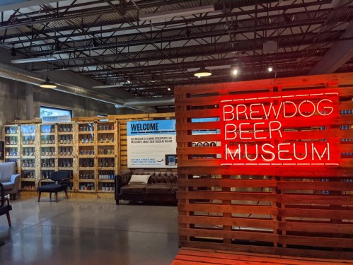 Interior of Brewdog Beer Museum featuring a neon sign, shelves of beer cans, and a cozy seating area.