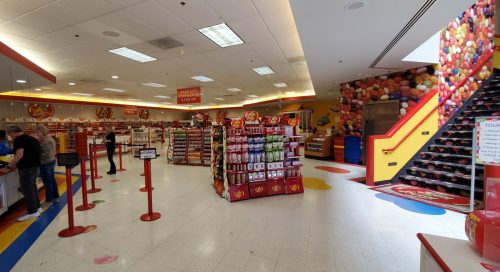A colorful candy store interior with shelves of sweets, a checkout area, and a staircase decorated with balloons.