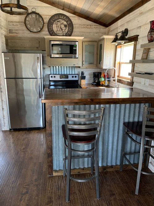 Cozy kitchen with stainless steel appliances, wooden accents, and a bar with metal stools in a rustic cabin setting.