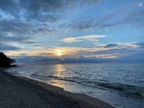 A serene beach at sunset, with gentle waves and a colorful sky filled with clouds.