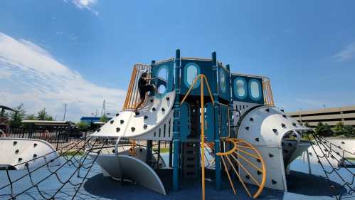 A colorful playground structure with climbing features under a clear blue sky, with a child playing on it.