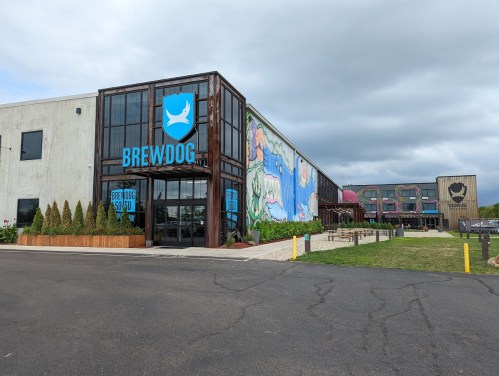 Exterior view of a BrewDog brewery with colorful murals and modern architecture under a cloudy sky.