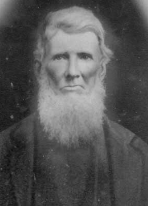 Black and white portrait of an older man with a long beard, wearing a dark coat and looking directly at the camera.