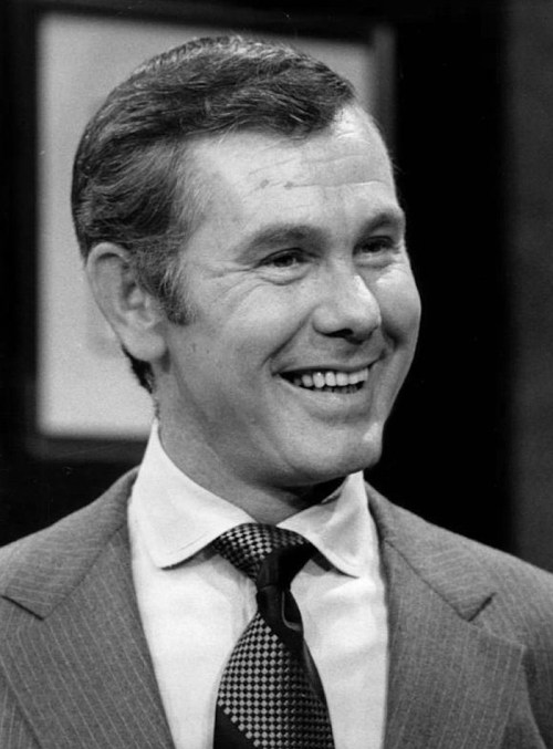 A smiling man in a suit and tie, captured in black and white, exuding a warm and charismatic presence.