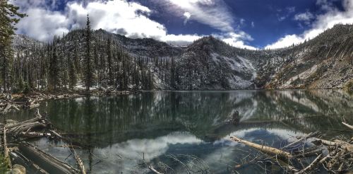 A serene mountain lake surrounded by snow-capped trees and rocky hills, reflecting the sky and landscape.