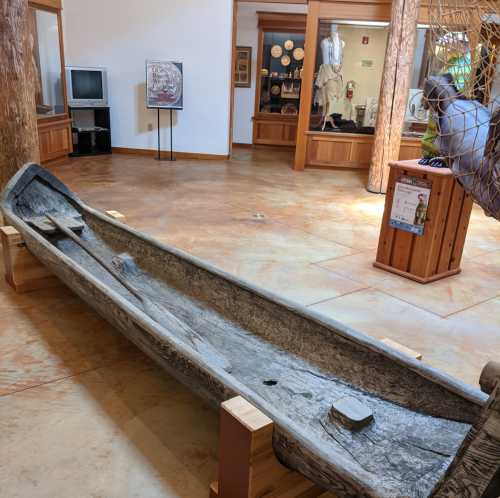 A traditional wooden canoe displayed indoors, surrounded by artifacts and exhibits in a museum setting.