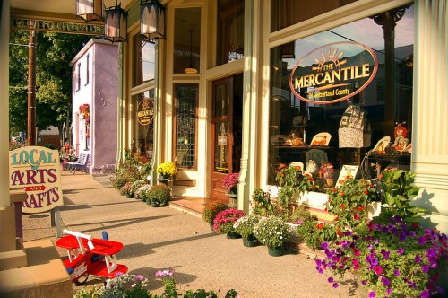 A charming storefront with flowers, a sign for local arts and crafts, and a vintage toy airplane on the sidewalk.