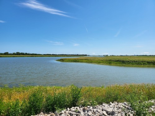 A serene landscape featuring a calm river, lush green banks, and a clear blue sky with a few clouds.