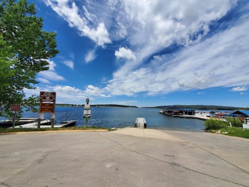 A scenic view of a lake with docks, under a blue sky with clouds, surrounded by greenery.