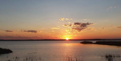 A serene sunset over a calm lake, with vibrant orange and pink hues reflecting on the water's surface.