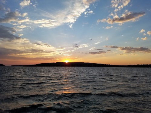A serene sunset over a calm lake, with colorful clouds reflecting on the water's surface.