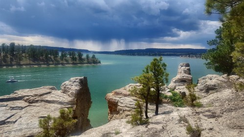 A scenic view of a lake surrounded by rocky cliffs and trees, with dark clouds looming overhead.
