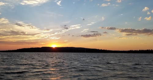 A serene sunset over a calm lake, with colorful clouds and a silhouette of distant hills.