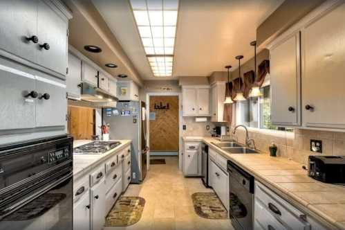 A modern kitchen with gray cabinets, stainless steel appliances, and a tiled floor, featuring a window and door to the outside.