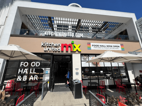 Exterior of Kitchen United Mix, featuring a food hall and bar, with outdoor seating and a bright, welcoming sign.