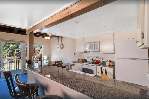 Bright kitchen with granite countertops, white appliances, and a bar area, opening to a deck with outdoor views.