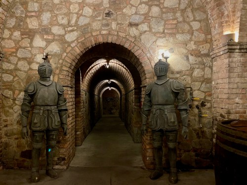 Two suit of armor figures stand at the entrance of a stone archway corridor, illuminated by soft lights.
