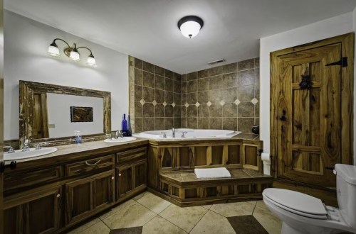 A spacious bathroom featuring a wooden vanity, a large jetted tub, and a rustic door with tile accents.