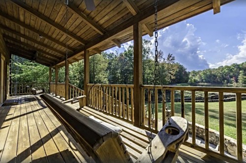 A wooden porch with swings overlooks a lush green landscape and a serene body of water under a blue sky.