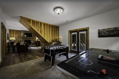 A cozy game room featuring a foosball table, air hockey table, and wooden staircase in a rustic setting.