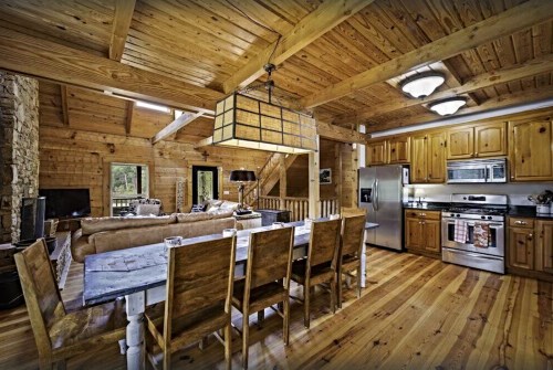 Cozy wooden cabin interior featuring a dining table, kitchen, and living area with rustic decor and warm lighting.